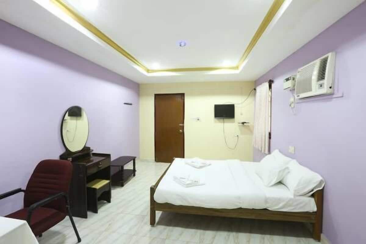 A bedroom with a bed, a desk, a chair, a mirror, and an air conditioning unit.