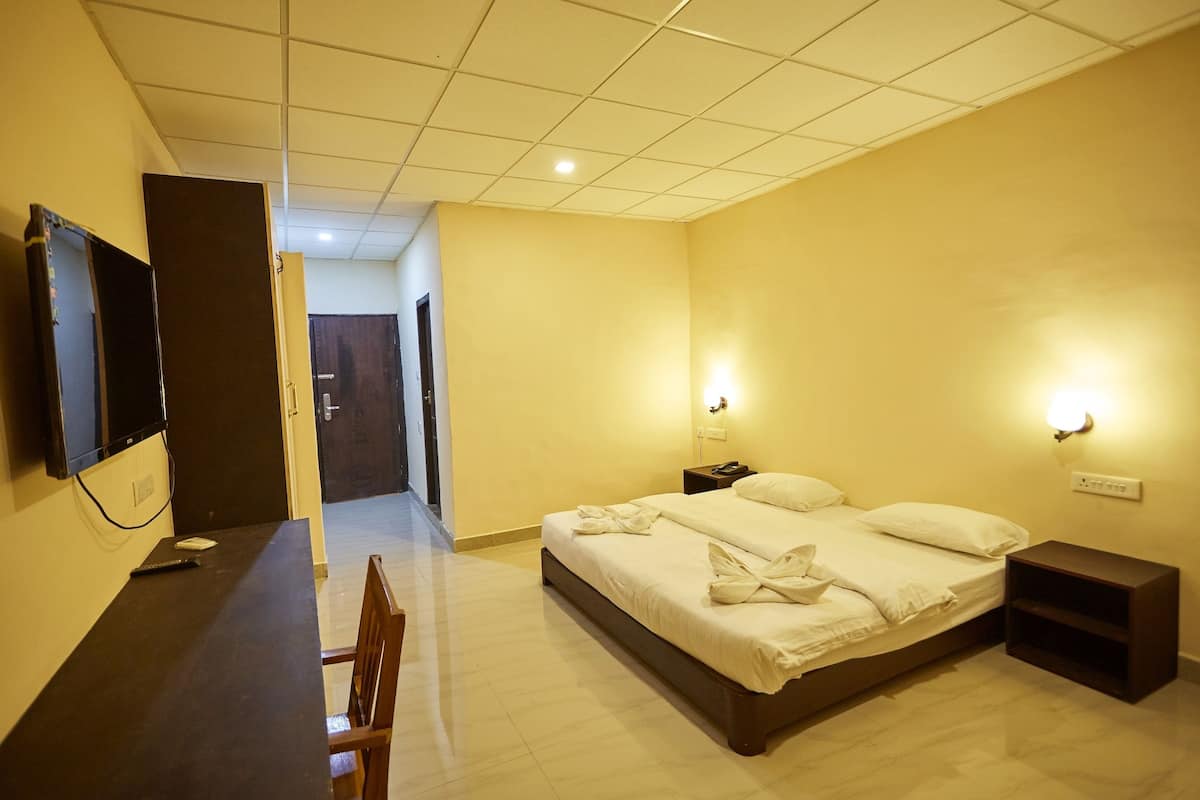 A hotel room with a bed, bedside tables, a desk with a chair, a TV, and a door leading to another room.