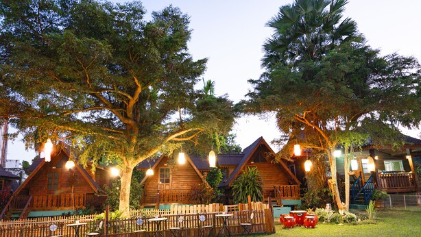 A rustic wooden cabin with multiple rooms, a fenced patio area with tables and chairs, and a staircase leading to the upper level. - RoomQuest Golden Triangle Premium Collection (Chiang Saen)