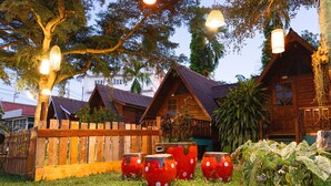 A wooden cabin with a sloped roof, surrounded by a wooden fence and a grassy yard. - RoomQuest Golden Triangle Premium Collection (Chiang Saen)
