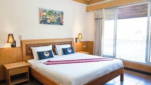 A hotel room with a wooden bed, two bedside tables, a large window with curtains, and a fruit-themed wall art piece. - RoomQuest Golden Triangle Premium Collection (Chiang Saen)