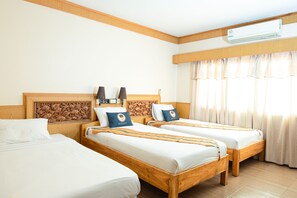 A hotel room with two wooden beds, a headboard with a carved design, a wall-mounted air conditioner, and a window with curtains. - RoomQuest Golden Triangle Premium Collection (Chiang Saen)