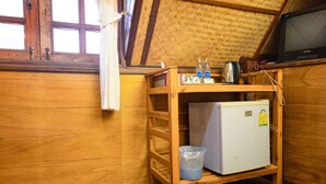 A wooden-framed room with a small white refrigerator, a wooden shelf with bottles and a kettle, and a television on a wooden stand. - RoomQuest Golden Triangle Premium Collection (Chiang Saen)