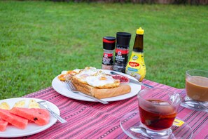 A picnic setup with a plate of food, a glass of tea, and condiments on a table outdoors. - RoomQuest Golden Triangle Premium Collection (Chiang Saen)