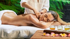 A massage therapy session in a spa setting with a client lying on a massage table, a therapist attending to the client, and a table with essential oils and a wooden block. - RoomQuest Golden Triangle Premium Collection (Chiang Saen)