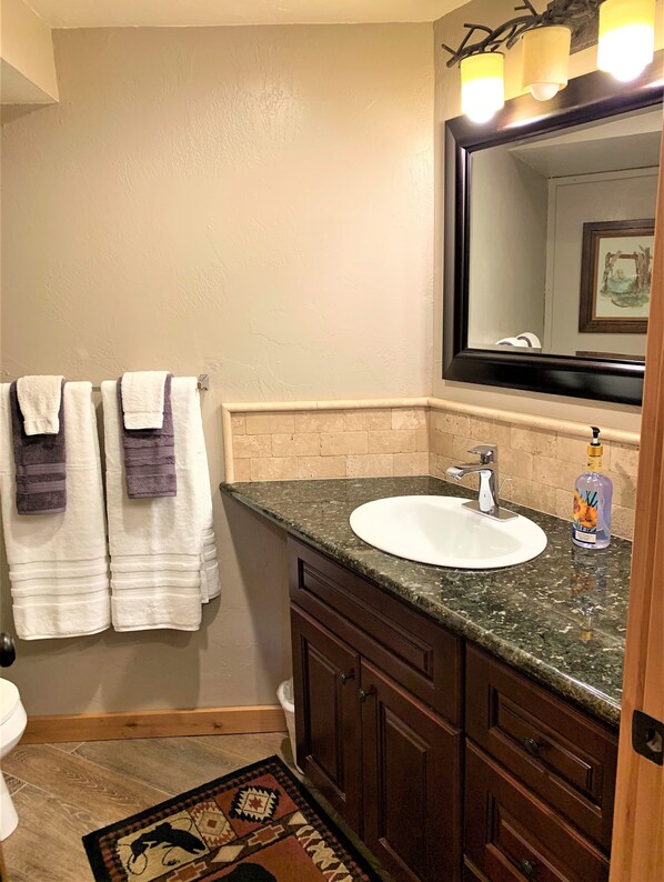 A bathroom with a white sink, dark wooden cabinets, a marble countertop, and a mirror with three lights.
