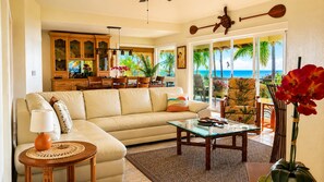 A living room with a sofa, coffee table, and a view of the ocean through large sliding doors.