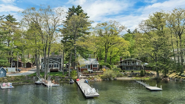 A lakefront property with docked boats, a pier, and houses surrounded by trees.