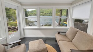 A sunroom with a view of a lake, a sofa, and a small table.