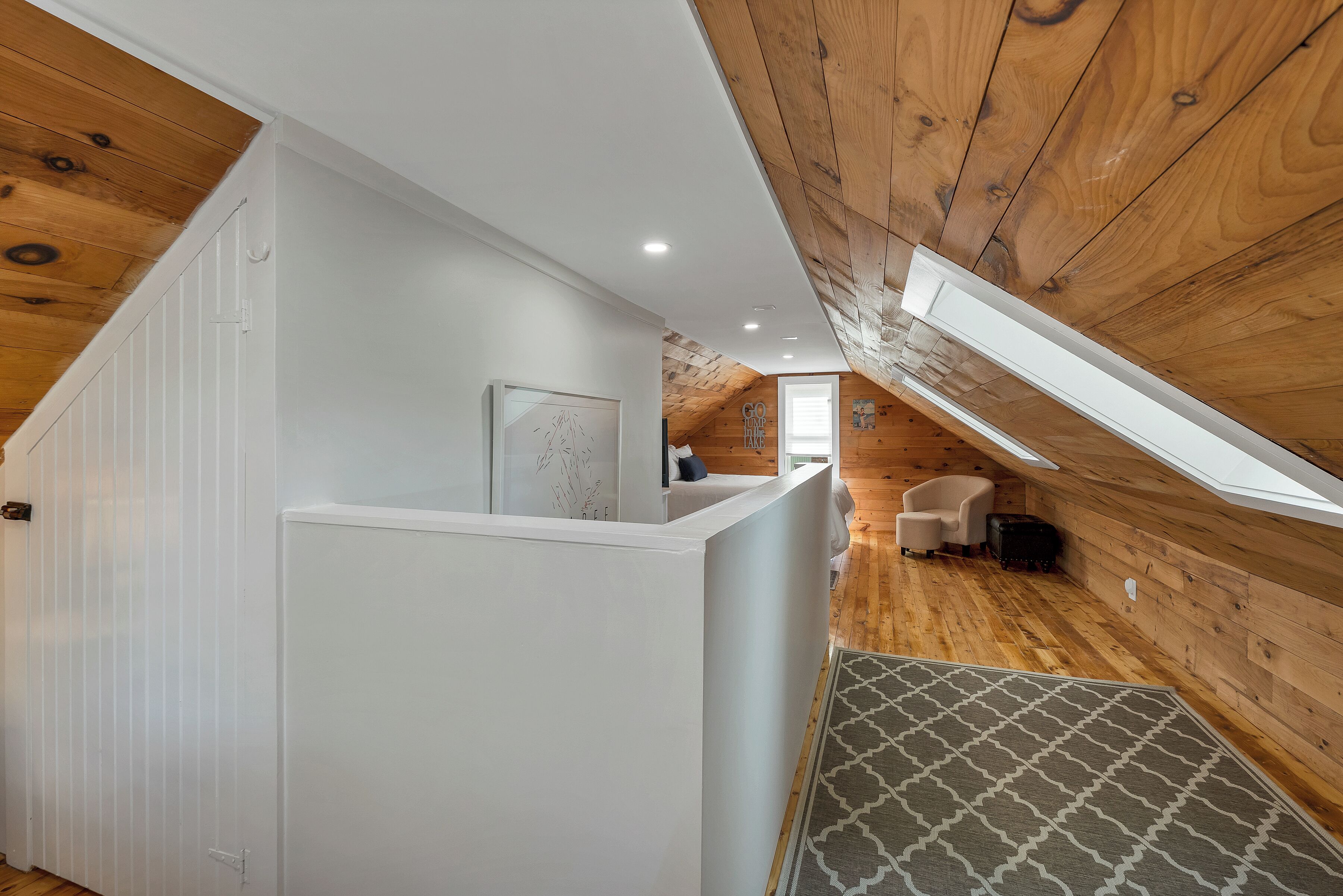 Une pièce de style « loft », avec des poutres en bois, une cloison blanche, un tapis à motifs et un petit coin salon.