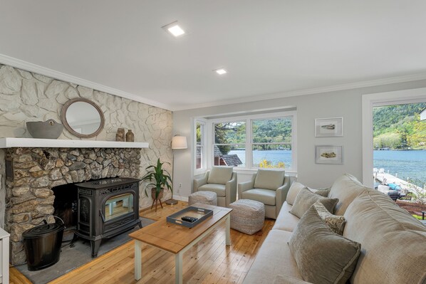 A living room with a stone fireplace, a wooden coffee table, a beige sofa, and a view of a lake.