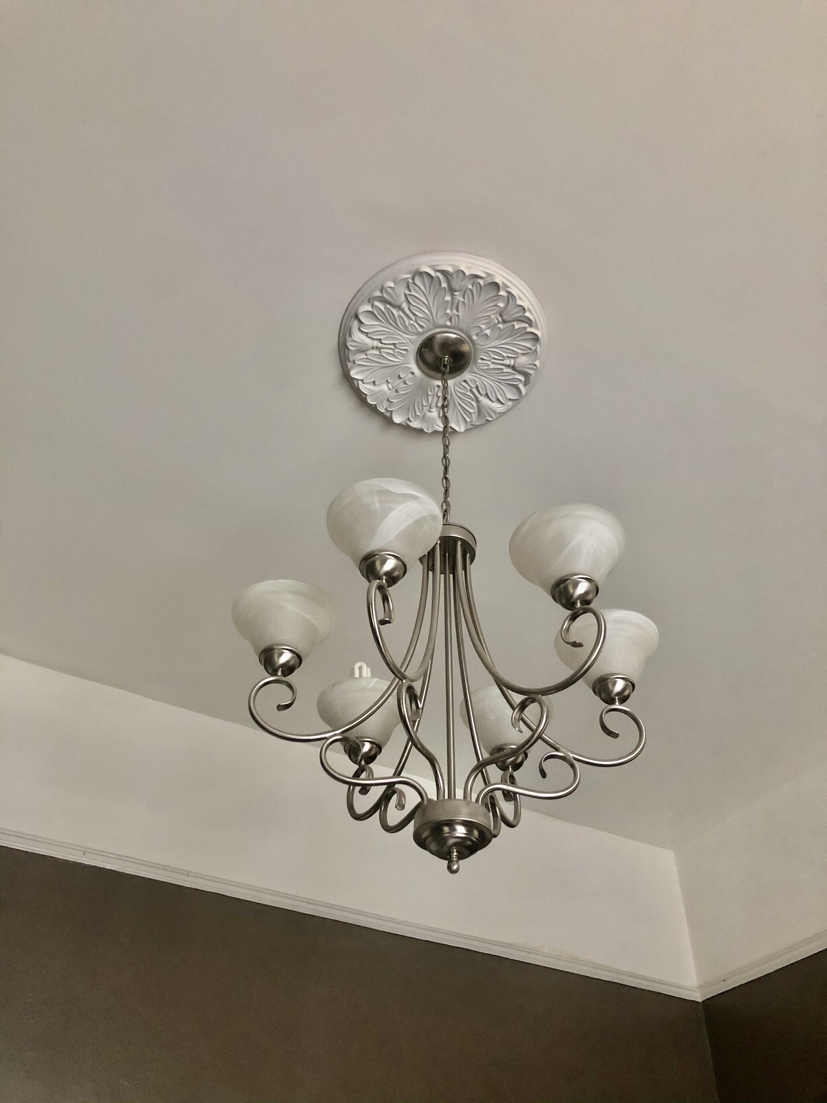 Un candelabro con una placa decorativa central y múltiples brazos con pantallas de vidrio esféricas.