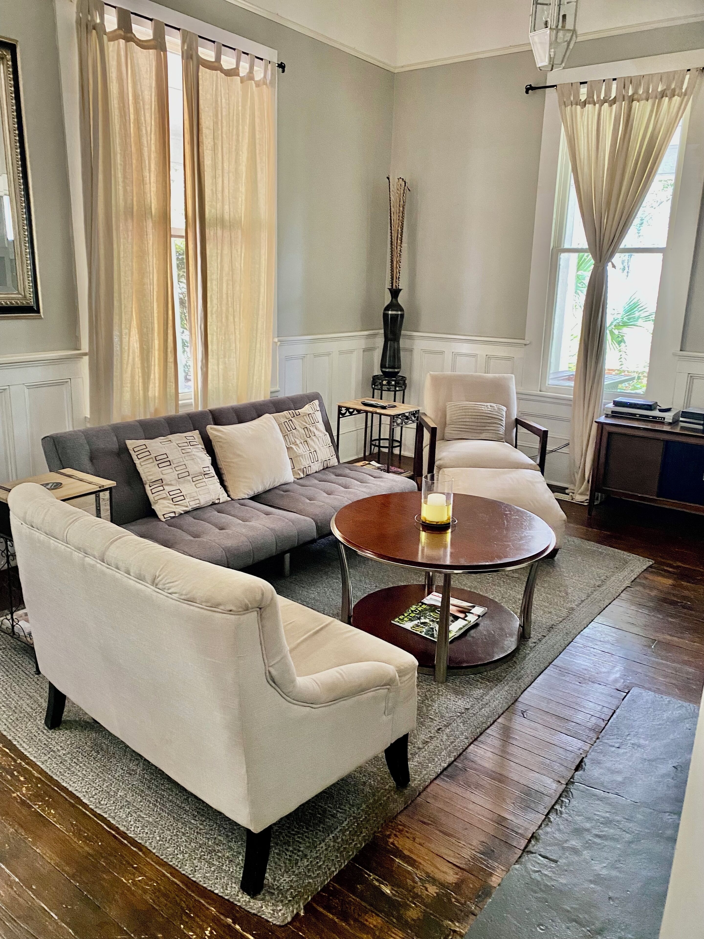 Una sala de estar con un sofá gris, un sillón blanco, una mesa redonda y una mesita de noche con un jarrón.