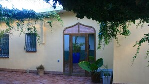 A courtyard with a tiled floor, a door with a decorative arch, and potted plants.