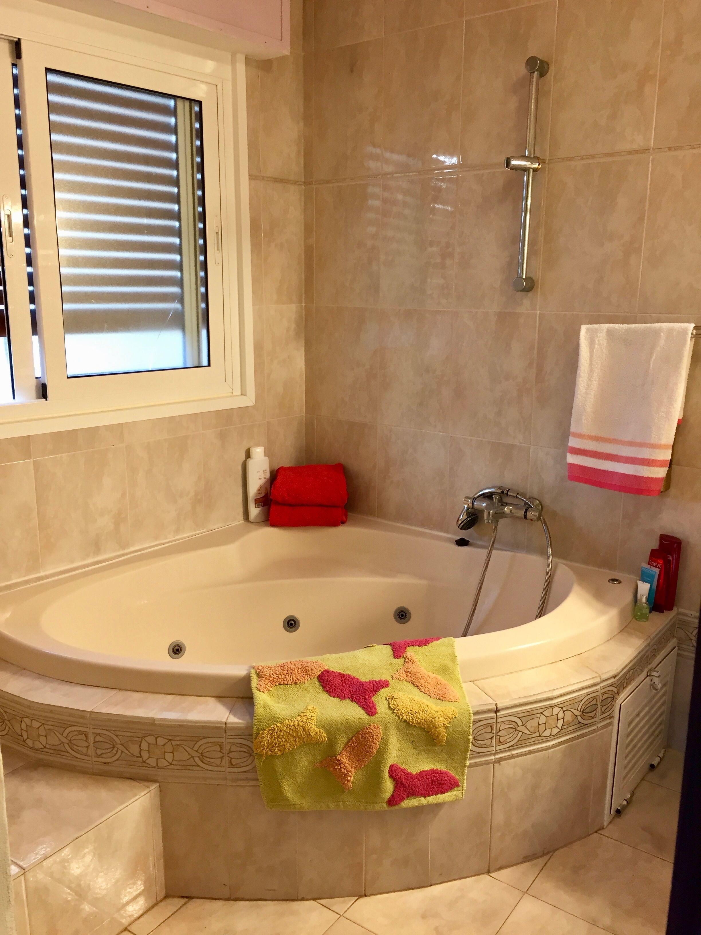 A bathroom with a freestanding bathtub, a showerhead, and a window with blinds.