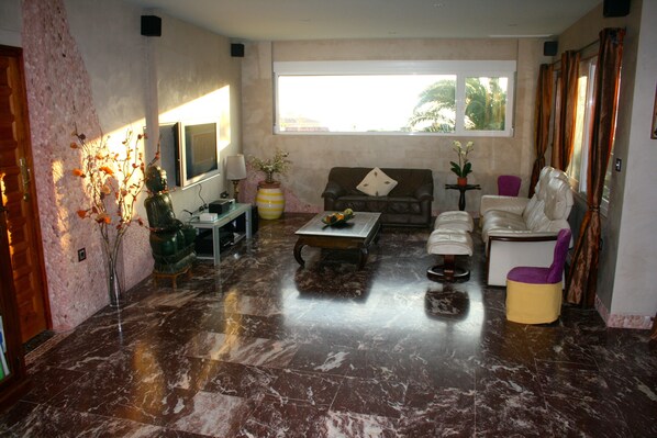 Un salón con suelo de mármol, un sofá, una mesa de centro y un televisor.