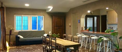 A dining area with a wooden table and chairs, a sofa, and a kitchen area with a counter and stools.