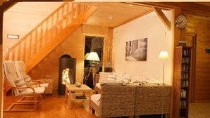 A cozy living room with a wooden staircase, wicker furniture, a fireplace, and a bookshelf. - LE CABANON BRETON - Ecogîte with SWIMMING POOL near SAINT-MALO, MONT-ST-MICHEL (Saint-Pierre-De-Plesguen)