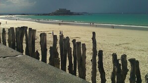 A beach with wooden posts in the foreground, a sandy shore, and a distant structure on the water. - LE CABANON BRETON - Ecogîte with SWIMMING POOL near SAINT-MALO, MONT-ST-MICHEL (Saint-Pierre-De-Plesguen)