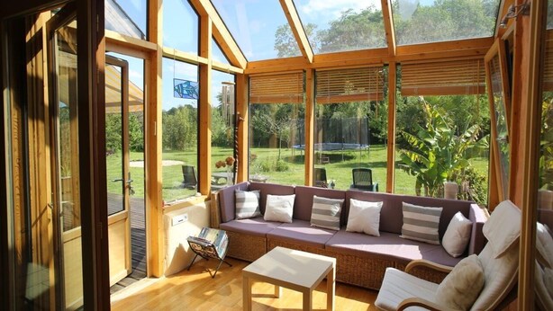 A sunroom with a wooden ceiling, a cushioned seating area, and a view of a garden. - LE CABANON BRETON - Ecogîte with SWIMMING POOL near SAINT-MALO, MONT-ST-MICHEL (Saint-Pierre-De-Plesguen)