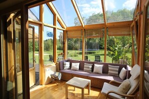 A sunroom with a wooden ceiling, a cushioned seating area, and a view of a garden. - LE CABANON BRETON - Ecogîte with SWIMMING POOL near SAINT-MALO, MONT-ST-MICHEL (Saint-Pierre-De-Plesguen)