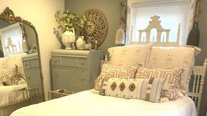 Un lit bien fait, avec une literie blanche, une commode avec un miroir et un élément décoratif mural.