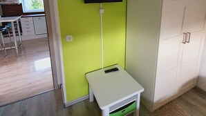 Une pièce avec un mur vert, un téléviseur fixé au mur, une table blanche avec un tiroir et une armoire blanche.