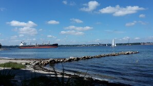 Un port où se trouvent un grand navire de transport de marchandises, un voilier et une côte rocheuse.