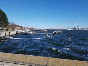 Une jetée bordant le rivage, avec des quais, un ciel dégagé et une usine industrielle visible au loin.