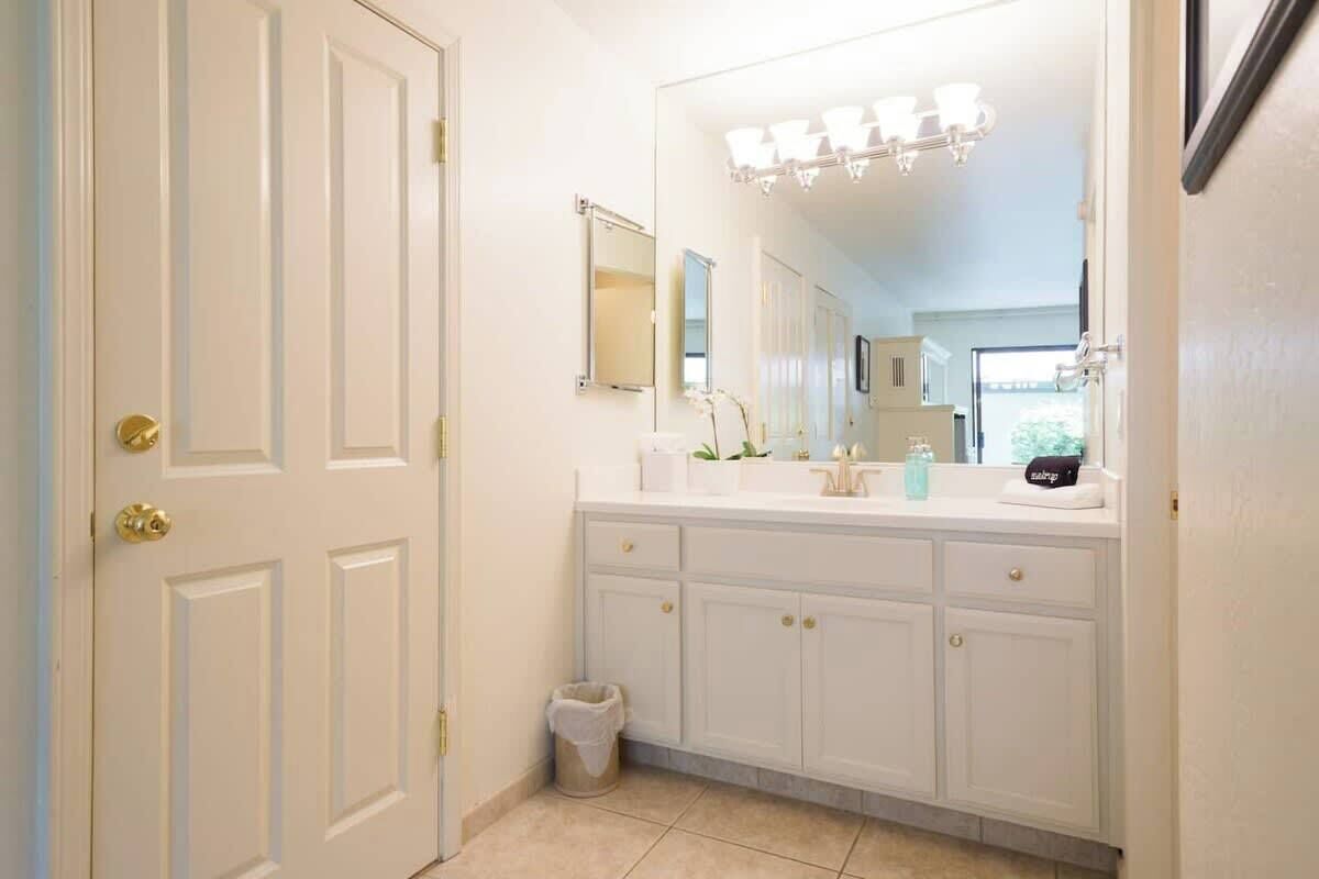 Une salle de bain avec des meubles blancs, un grand miroir et un meuble-lavabo avec un évier.