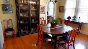 Une salle à manger avec une table et des chaises en bois, un buffet aux portes vitrées et une fenêtre avec des stores.