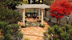Un jardin avec un sentier en pierre, un kiosque et un arbre aux feuilles rouges.