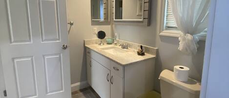 A bathroom with a white door, a sink with a mirror above it, a toilet, and a trash bin.