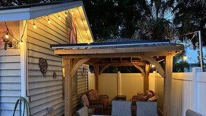 Une terrasse couverte avec une table et des chaises en bois, des guirlandes lumineuses et un drapeau américain.