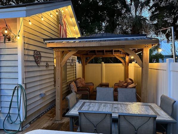 A covered patio with a wooden table and chairs, string lights, and an American flag.