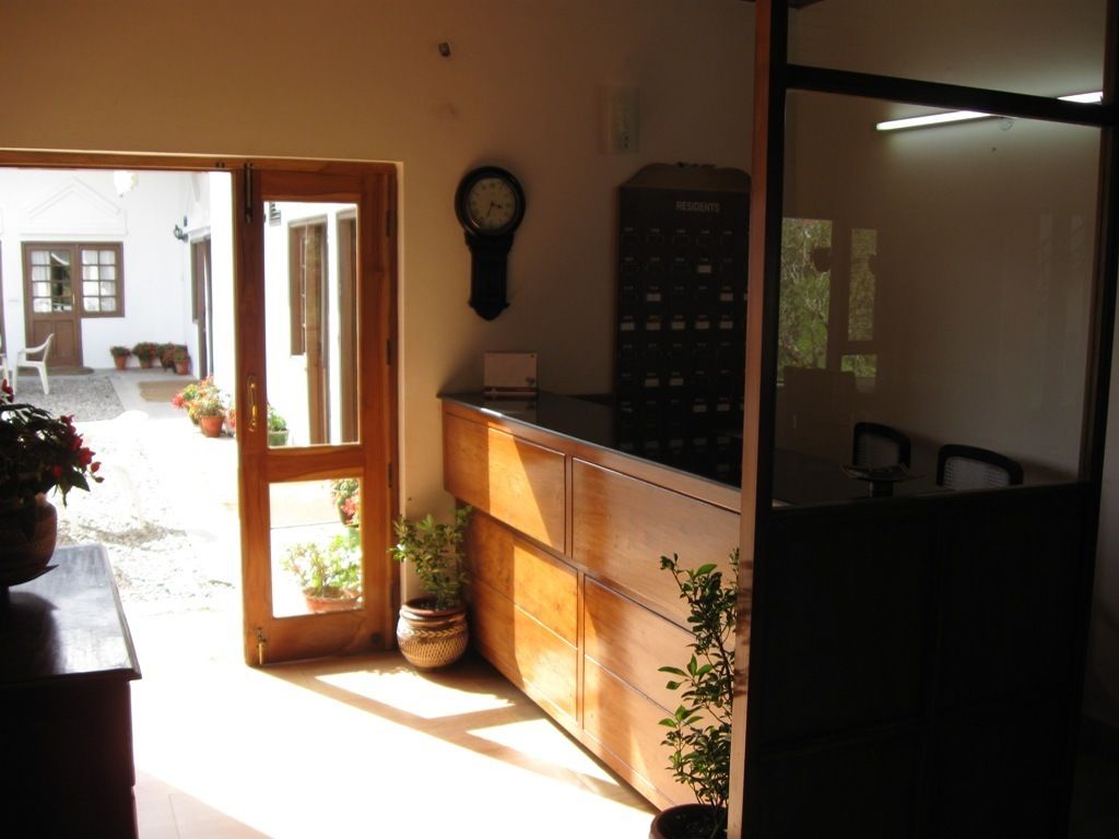 A room with a wooden cabinet, a clock on the wall, and a door leading to an outdoor area with potted plants.