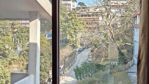 Une vue depuis une fenêtre donnant sur une rue bordée d’immeubles et d’arbres, avec un ciel dégagé.