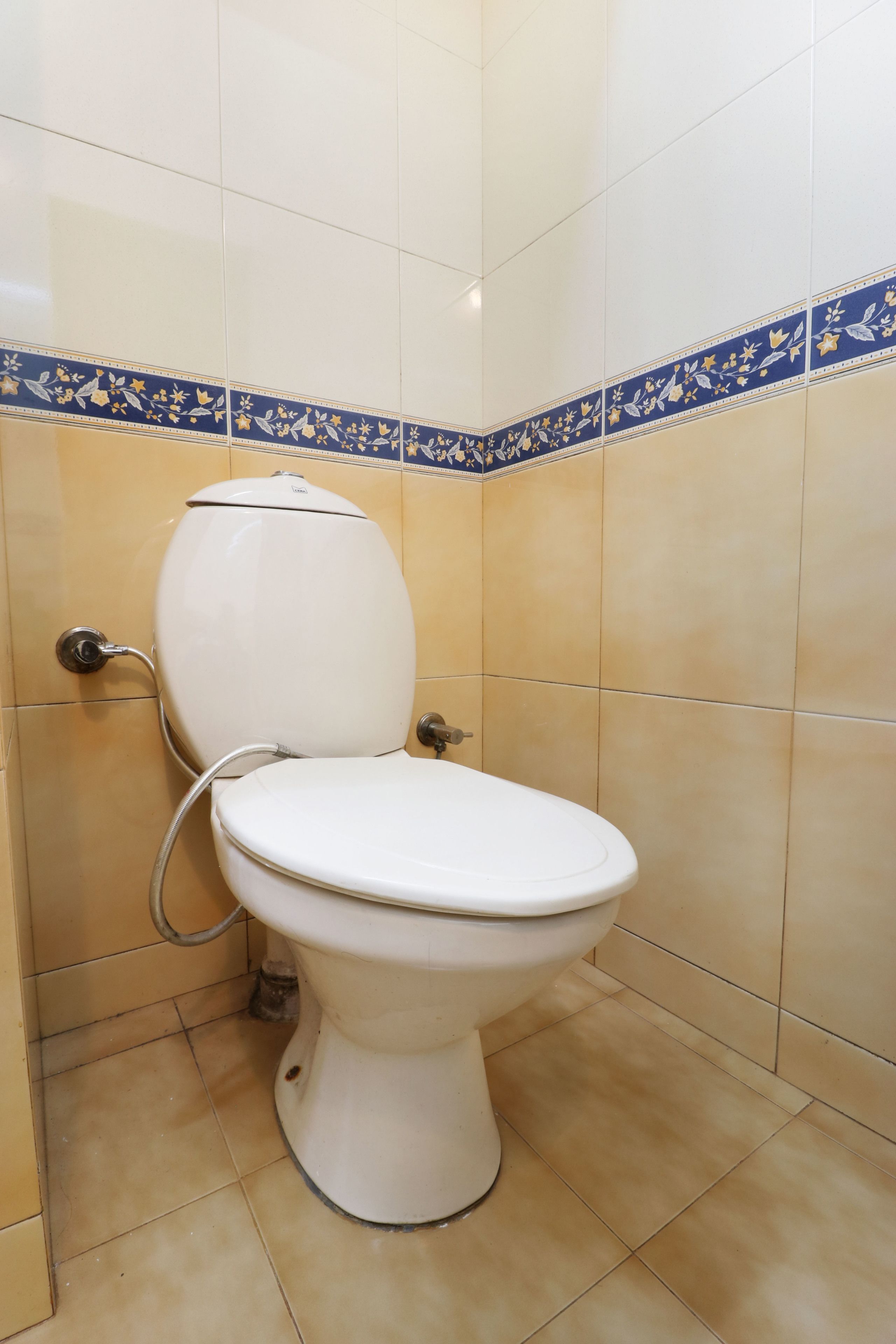 A toilet in a bathroom with beige tiles and a blue decorative border.