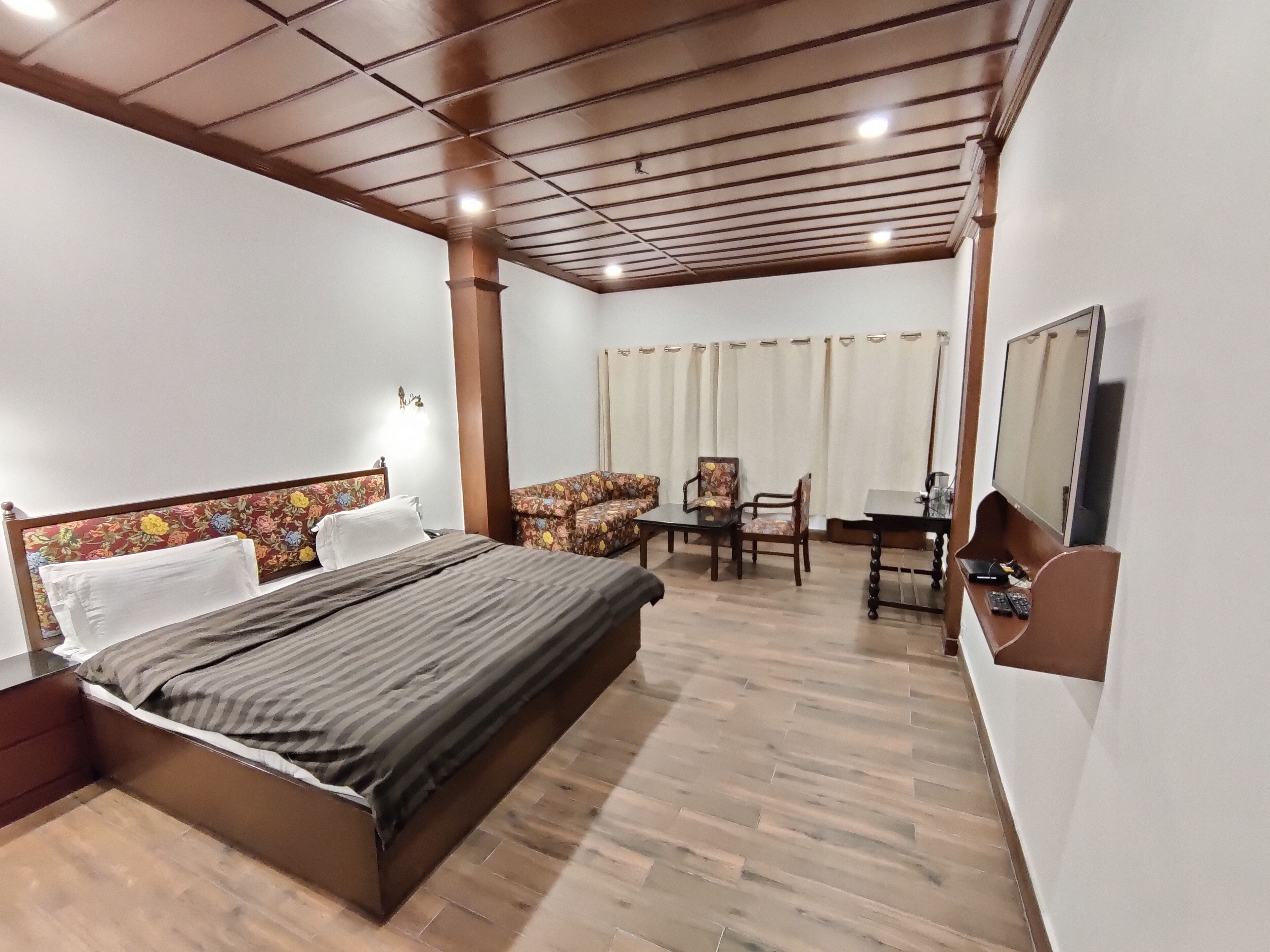A hotel room with a bed, a desk, two chairs, a television, and a window with curtains.