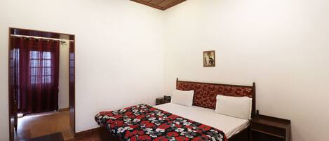 A bedroom with a bed, a nightstand, a wooden headboard, a small table, and a window with curtains.