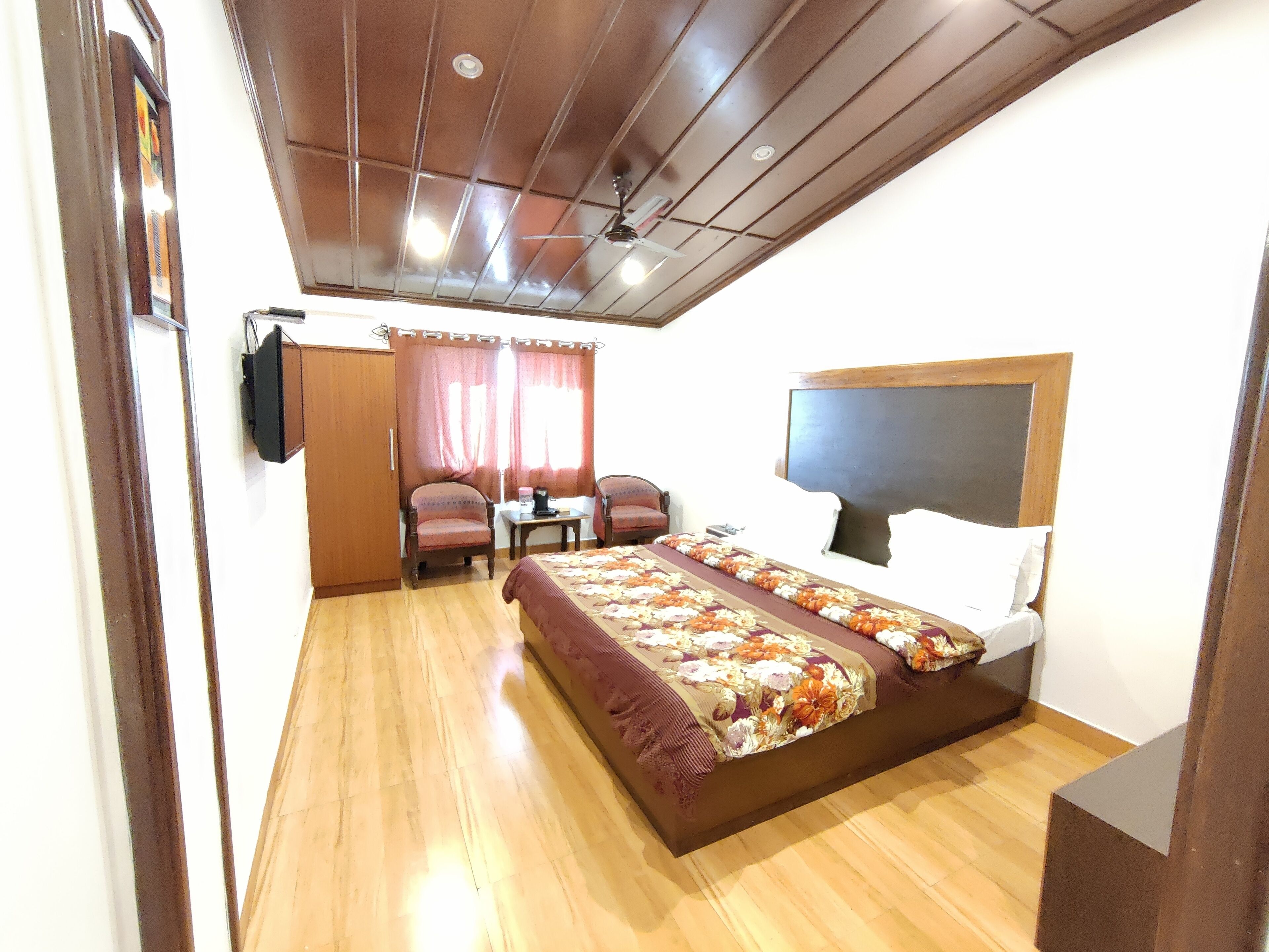 Un dormitorio con techo de madera, una cama con colcha estampada, un escritorio con silla y un televisor fijado a la pared.