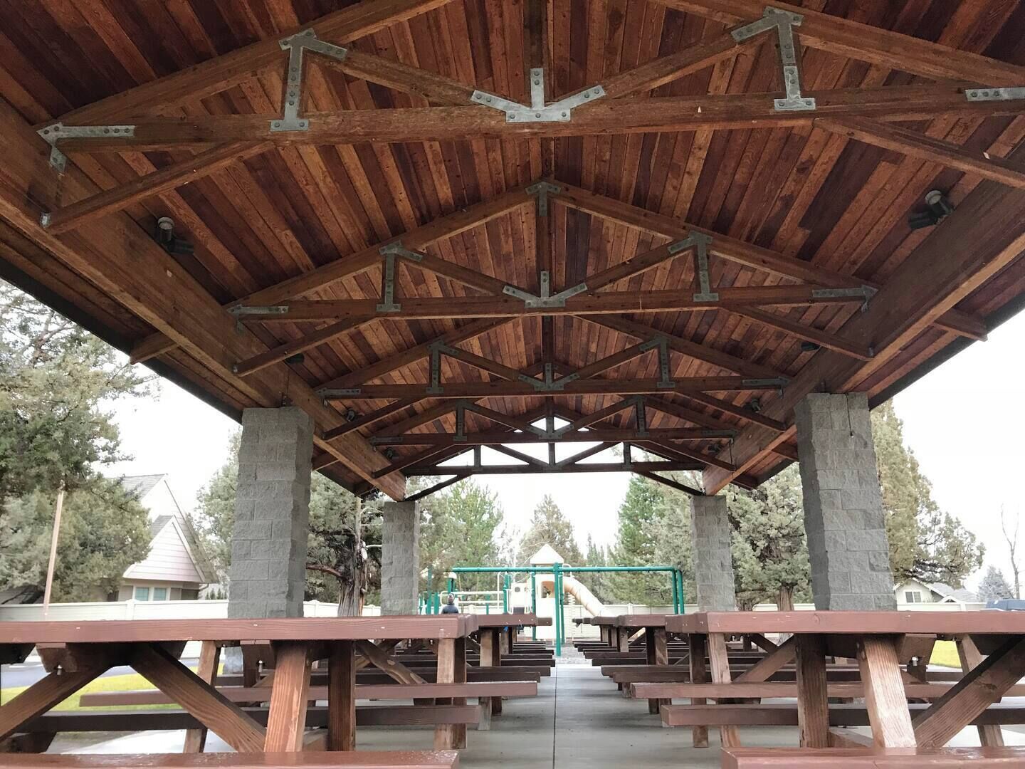A covered picnic area with wooden benches and a metal frame structure.