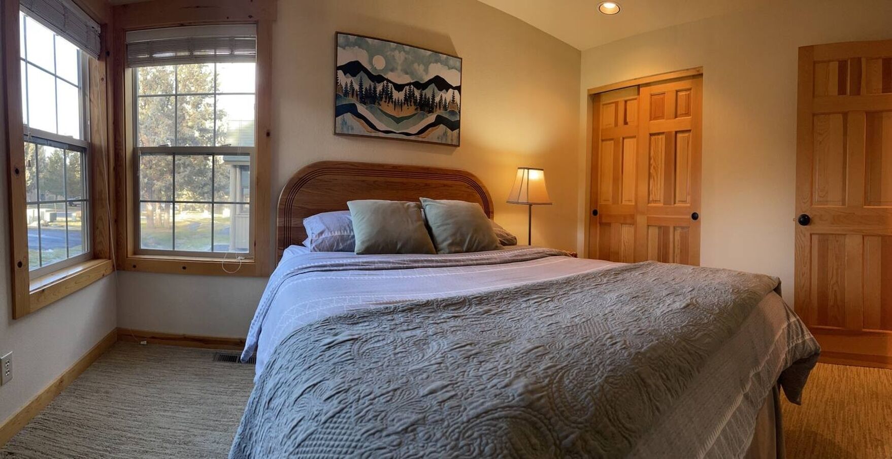 A bedroom with a large bed, a window, a painting, and wooden doors.