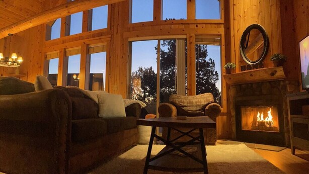 A cozy log cabin interior with a fireplace, large windows, and a comfortable seating area. - Cozy knotty pine chalet with creekside deck, BBQ, and access to pools, hot tubs, gym, golf, hiking. (Redmond)