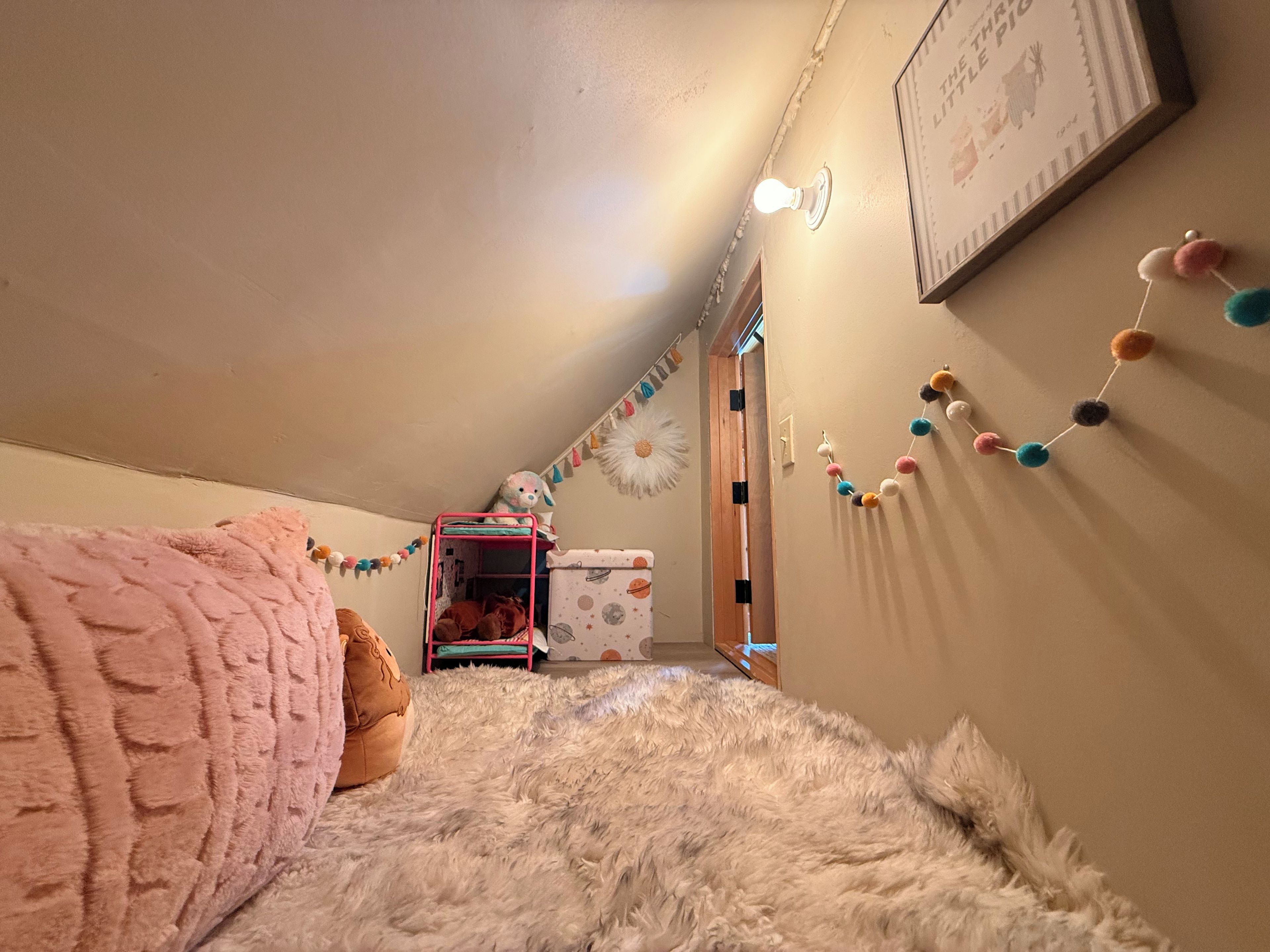 Una camera accogliente con un letto a castello, biancheria soffice, un portalampada a parete e una ghirlanda decorativa di pon pon.