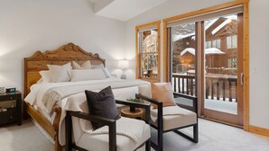 Ein Schlafzimmer mit einem Holz-Kopfteil, einem großen Bett, zwei Stühlen, einem Nachttisch und einer Glasschiebetür, die zu einem Außenbereich führt.