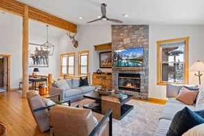 A spacious living room with a stone fireplace, wooden beams, and a large TV. - A/C, Private Salt Water Hot Tub, Outdoor Pool, Deck, Grill, Garage (Steamboat Springs)