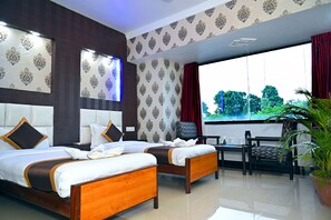 A hotel room with two beds, a TV, a window with curtains, a chair, and a potted plant. - Hotel Rajhans International (Bhagalpur)