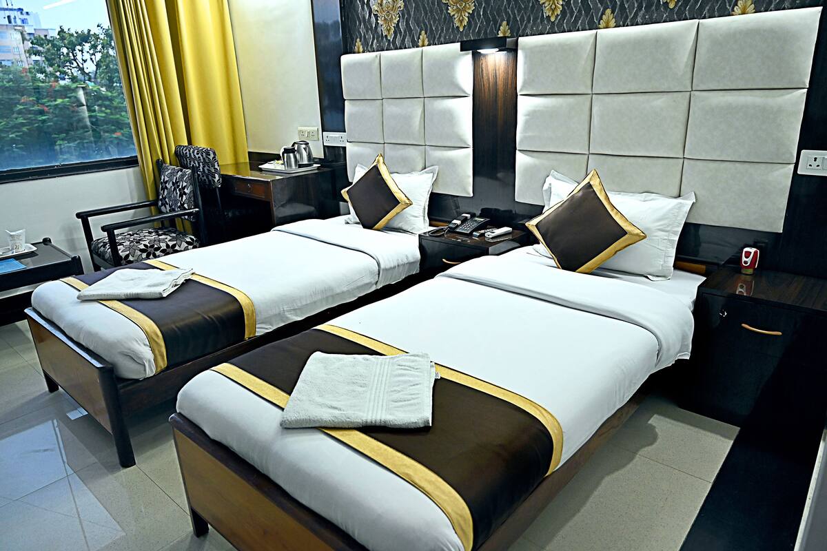 Une chambre d’hôtel avec deux lits, une table de chevet, une chaise et une fenêtre avec des rideaux.