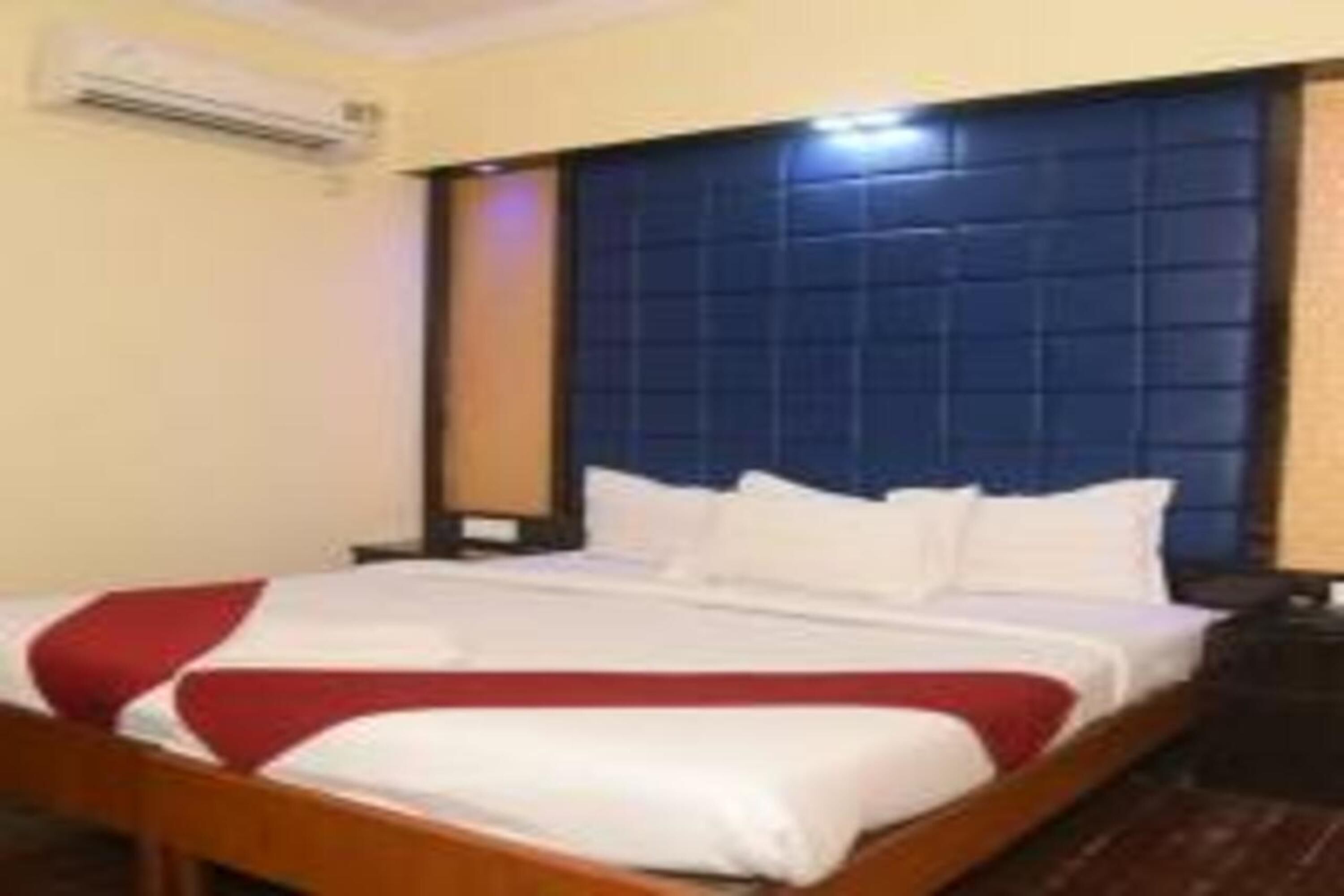 Habitación de hotel con una cama grande, cabecera de madera y almohada roja decorativa.